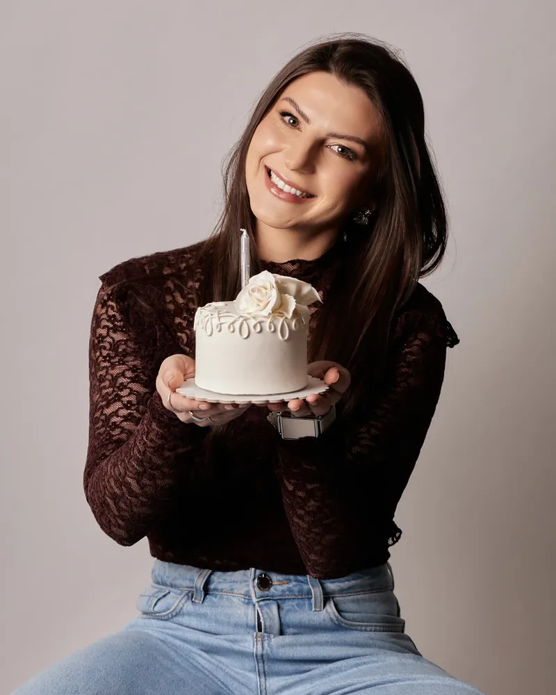 Mulher sorrindo segurando um bolo branco pequeno com vela, em ensaio de aniversário em estúdio, em Curitiba