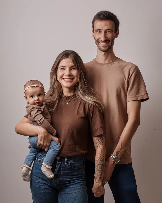 Casal sorrindo com a filha bebê no colo, em ensaio de família em estúdio, em Curitiba