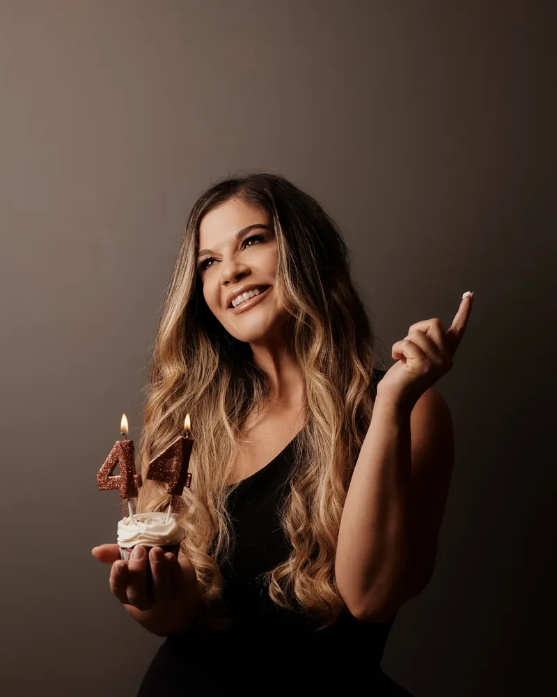 Mulher sorrindo com velas em forma do número 44 sobre um cupcake, em ensaio de aniversário com luz suave